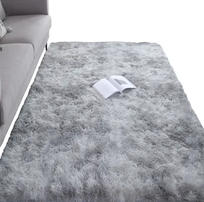 A fluffy gray rug is placed on the floor next to a gray sofa. An open book rests on the rug.