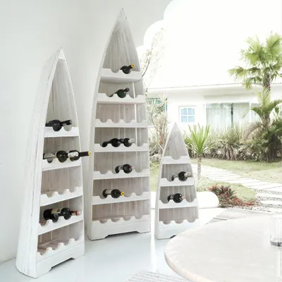 Three white wooden wine racks shaped like boats are displayed outdoors in front of a house with a garden.