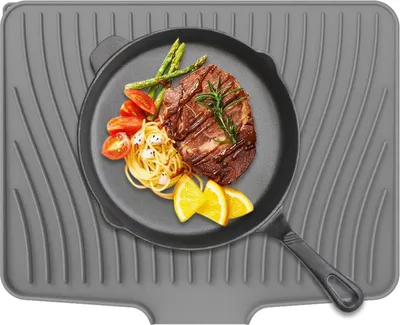A cooked meal is presented on a black plate, which is placed on a gray silicone drying mat. The meal consists of a steak, spaghetti, asparagus, cherry tomatoes, and orange slices.