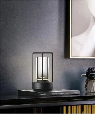 A modern table lamp is placed on a shelf next to a book and a decorative flower.