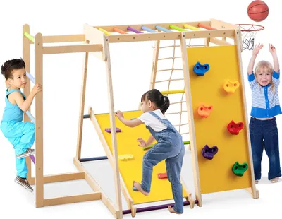 Children playing on a wooden indoor climbing frame with a slide, climbing wall, rope ladder, and basketball hoop.