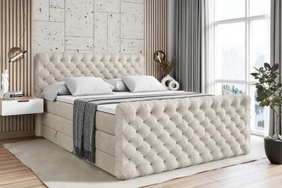 A tufted beige boxspring bed with white pillows and a gray throw blanket is shown in a bedroom setting.