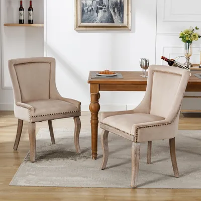 Two beige upholstered dining chairs are placed around a wooden dining table in a well-lit room.