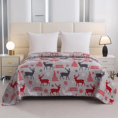A Christmas-themed blanket is spread across a bed with two pillows.