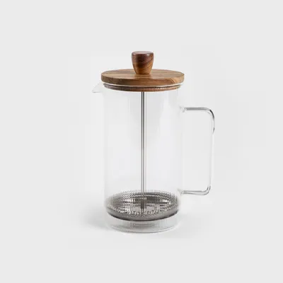 A glass French press with a wooden lid and handle, set against a plain background.