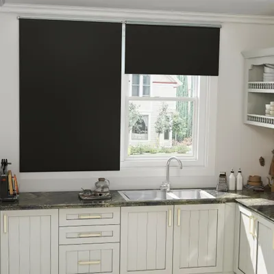A kitchen scene with a window covered by black roller blinds.