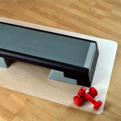 A fitness step and two dumbbells on a mat on a wooden floor.