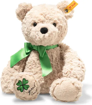 A beige teddy bear with a green ribbon and a clover leaf embroidered on its paw.
