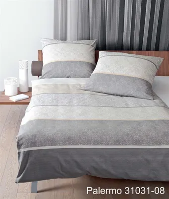 A bed with bedding set and pillows, with decorative vases on a side table.