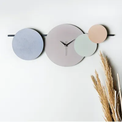 A modern wall clock with overlapping circular elements in muted colors, mounted on a white wall.