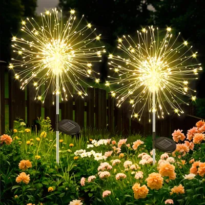 Two solar-powered dandelion-shaped lights illuminate a garden at dusk, surrounded by flowers.