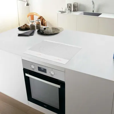 A modern kitchen island with a white countertop, featuring a built-in oven and an induction cooktop.