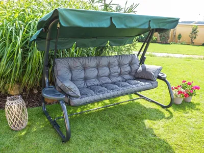A garden swing with cushions and a canopy, set on a grassy lawn.