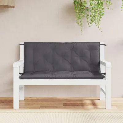 A dark gray bench cushion is placed on a white wooden bench. The background is a light-colored wall with some hanging greenery.