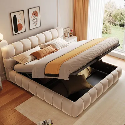 A tufted beige bed frame with the mattress lifted to reveal storage space underneath, in a well-lit bedroom.