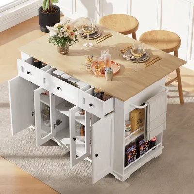A white kitchen island with a wooden countertop is shown in a room with natural light. The island has open doors and drawers, revealing shelves stocked with jars and boxes. Two wooden stools are placed at the countertop.