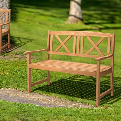A wooden garden bench sits on grass next to a stone path, with trees in the background.