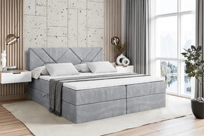 A modern bedroom with a large gray boxspring bed as the focal point, set against a textured wall and large windows with a scenic view.