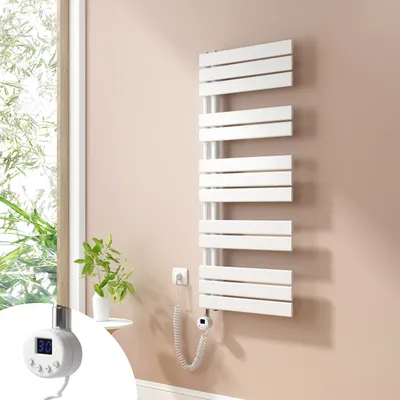 A white electric towel radiator is mounted on a light beige wall next to a window with greenery visible outside. A small white side table with a plant is also present.