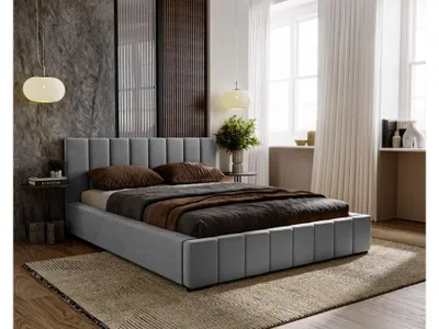 A bedroom scene featuring a gray upholstered bed with brown bedding, set against a textured wall and large windows with white curtains.