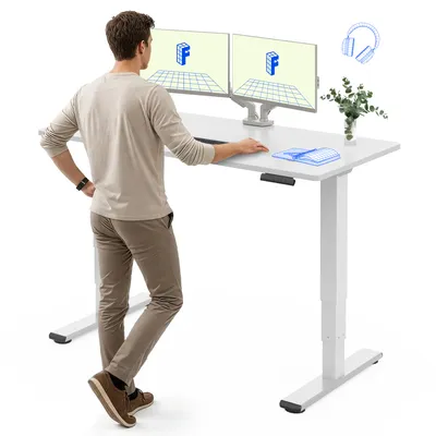 A man stands at a white standing desk with dual monitors.