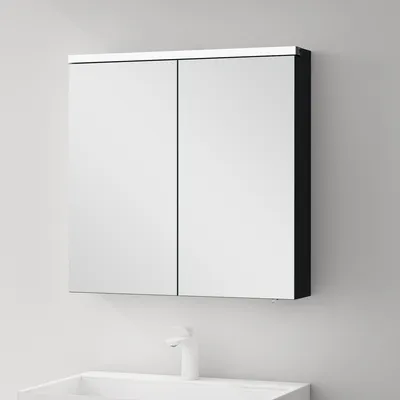A bathroom cabinet with mirrored doors is mounted on a light gray wall above a white sink and faucet.