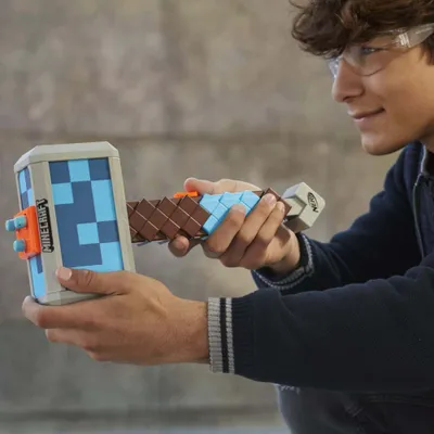 A young person wearing safety glasses is holding a Minecraft-themed Nerf hammer.
