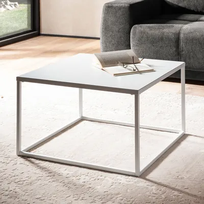 A white square coffee table with a book and glasses on it, placed on a textured rug in a living room setting.