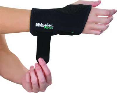 A person is wearing a black Mueller Greenline wrist brace on their left arm, and their right hand is adjusting a strap on the brace.