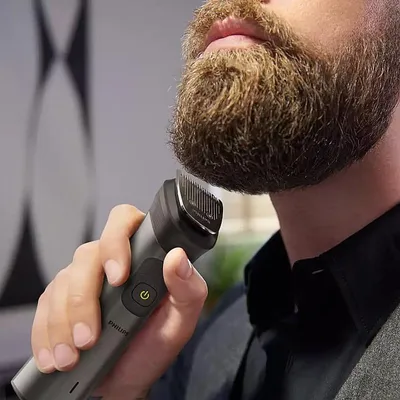 A man is trimming his beard with a Philips hair clipper.