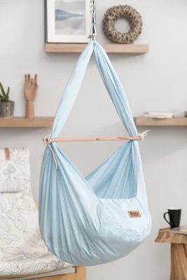 A baby hammock is hanging in a room with shelves in the background.