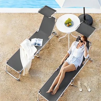 Two lounge chairs by a pool with a woman relaxing on one of them.