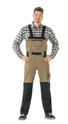 A man wearing a plaid shirt and tan and black overalls stands against a white background.
