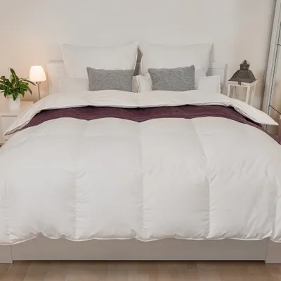 A neatly made bed with a white duvet and purple throw blanket.