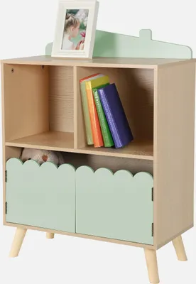 A light wood children's bookshelf with a light green decorative top edge and two light green cabinet doors at the bottom. A framed picture sits on top of the bookshelf. Several colorful books are on the middle shelf, and a stuffed animal is visible behind 