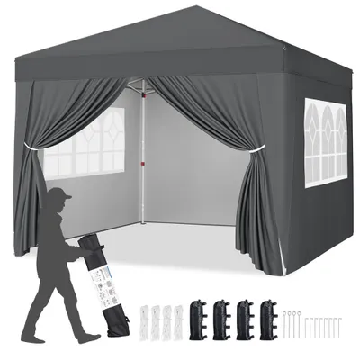 A dark gray pop-up canopy tent is shown with its sides open, revealing the interior. A silhouette of a person is standing to the left, holding a rolled-up bag. Several accessories are laid out in the foreground.