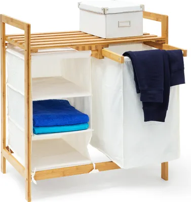 A bamboo laundry basket with fabric compartments and shelves, holding folded towels and dark clothing.
