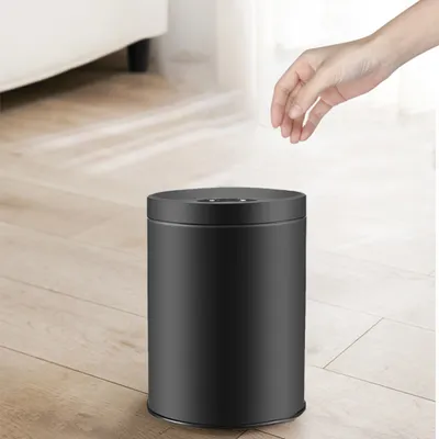 A hand is about to drop something into a black trash can.