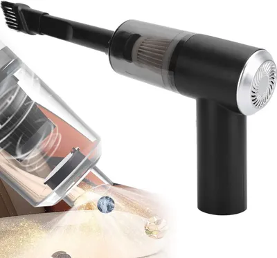 A black and transparent handheld vacuum cleaner with a brush attachment, shown in use cleaning dust and glitter from a surface.