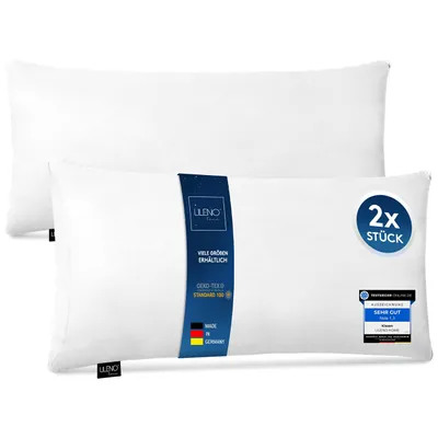Two white pillows are shown, one in front of the other. The front pillow has a blue label with text and logos.