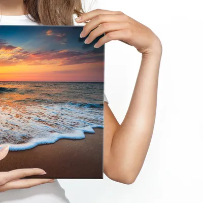 A person is holding a canvas print of a beach sunset.