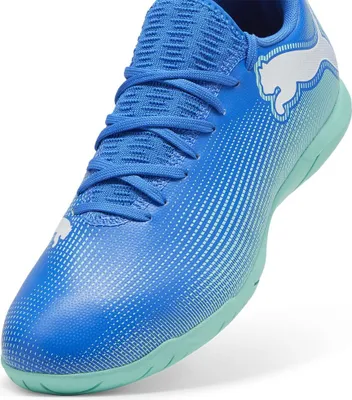 A close-up, studio shot of a blue Puma soccer shoe with white accents and a light green sole.