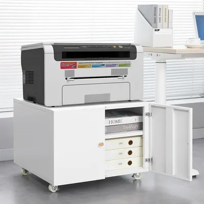 A white mobile printer stand with drawers and a cabinet door, holding a printer and some books. The stand is placed on a floor next to a desk with a laptop.
