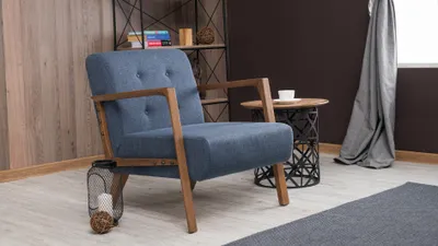 A blue armchair with wooden legs sits in a room with a bookshelf in the background.