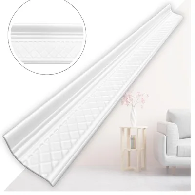 A white decorative molding strip is shown diagonally against a light gray and white background. A small side table with a vase and flowers, and a portion of a white sofa are visible in the background.