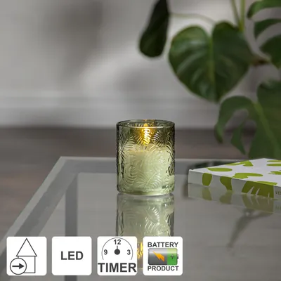 A decorative LED windlight with a leaf pattern sits on a glass table, with a plant in the background. Icons indicating features are displayed at the bottom.