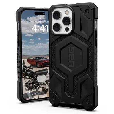 A black UAG Monarch protective case for an iPhone 14 Pro Max is shown, with the phone's screen displaying a motorcycle and a red car in a desert landscape.