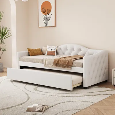 A white daybed with a pull-out trundle bed is shown in a room with a plant and artwork on the wall.