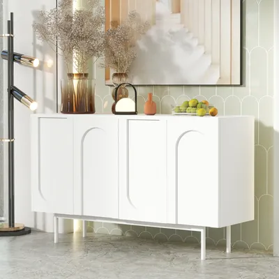 A white sideboard with four doors and arched detailing is displayed in a well-lit room with decorative items on top.