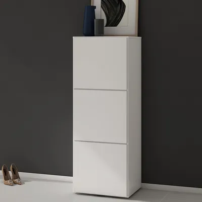 A white shoe cabinet with three drawers against a dark gray wall, with two pairs of shoes on the floor in front of it.